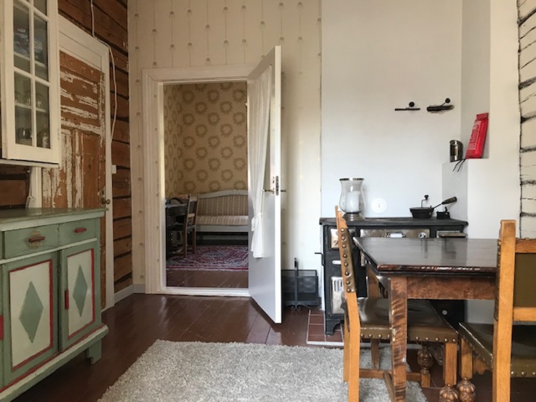 A cosy sitting room with a black wood stove, a painted antique cupboard, and a long dining table