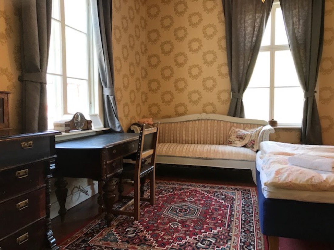 An antique writing desk and a striped settee beside a sunlit window — a quiet spot for a writers' retreat